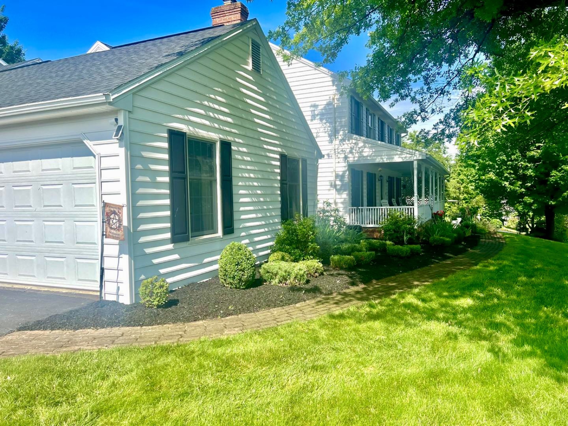 White colonial home with fresh mulch beds, trimmed shrubs, and a curved paver walkway, landscaping in Mt Holly Springs PA